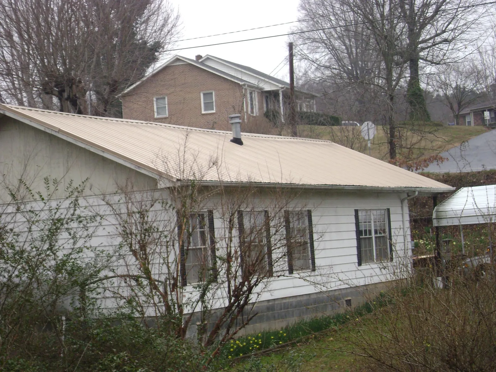 Tan metal roof on a white sided house set into a hillside — Commercial Roofing by Roofing Brothers in Maynard