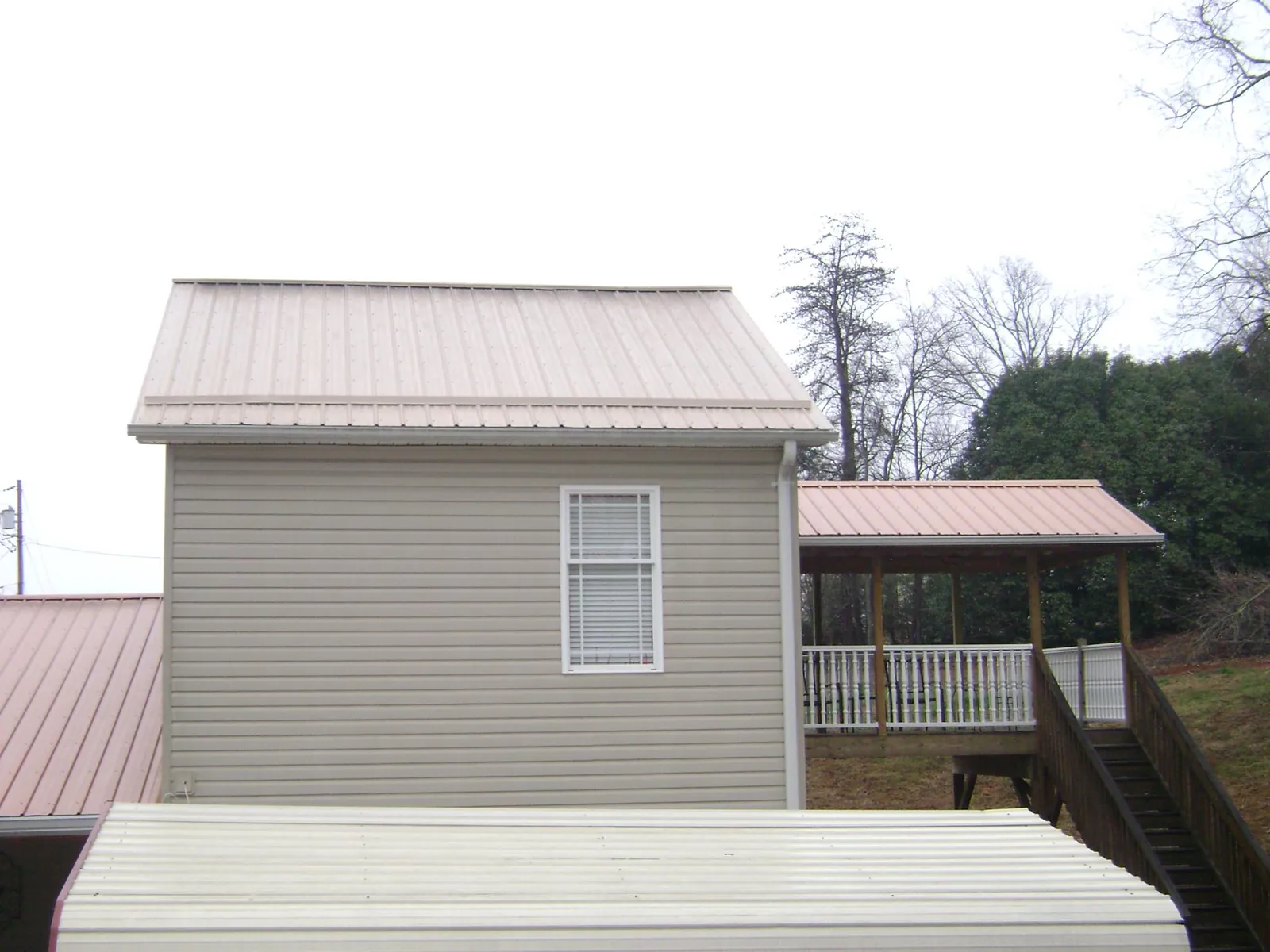 Tan metal roofs on a two story addition and attached porch, from a Roof Replacement job in Maynard